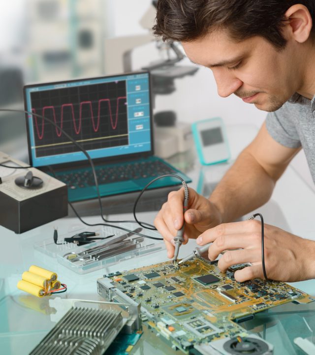 Young energetic male tech or engineer repairs electronic equipment in research facility. Shallow DOF, focus on the face of the worker.